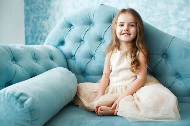 Великолепная маленькая девочка с темными светлыми волосами лежит на синем диване