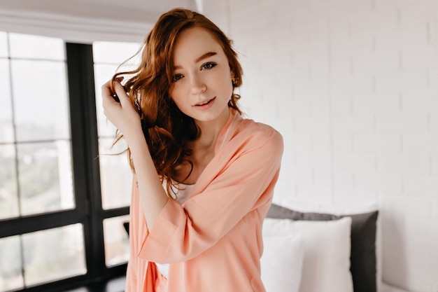 Gorgeous red-haired woman with cute smile posing at home. Graceful european girl standing in her flat.