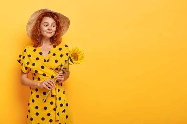 Gorgeous redhead woman posing in yellow polka dress and straw hat