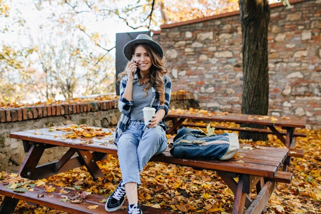 화려한 슬림 여성은 가을 날에 다리를 건너 테이블에 앉아 짧은 청바지를 착용
