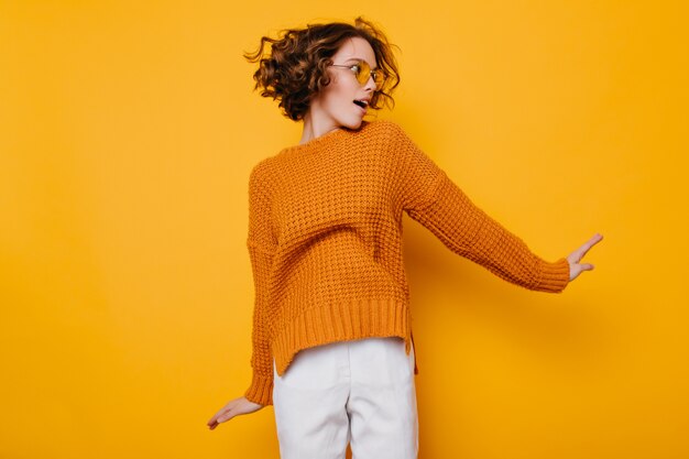 Gorgeous slim woman in white pants jumping on yellow background and looking away