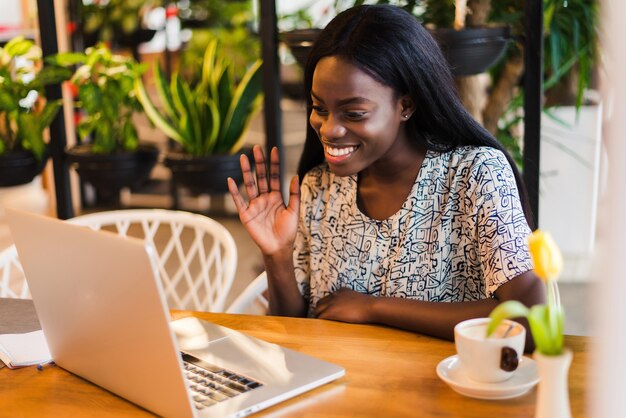 화려한 미소 짓는 여성은 커피 숍에서 레크리에이션을 즐기고 휴대용 노트북을 통해 화상 통화를하고 응용 프로그램을 사용합니다.