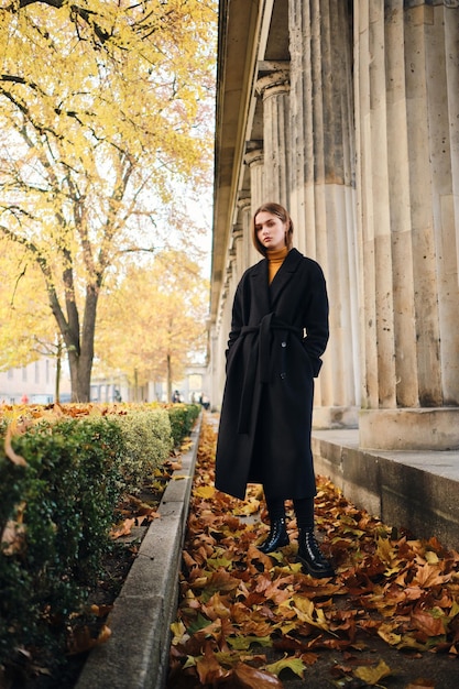 Splendida ragazza alla moda in cappotto nero che riposa nel bellissimo parco cittadino autunnale