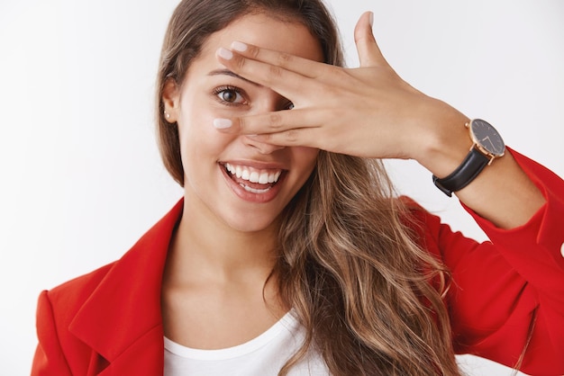 Gorgeous  stylish successful modern businesswoman in red trendy jacket smiling  making funny gestures hiding  eyes behind palm