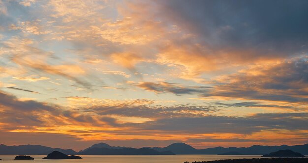 海の上の雲と豪華な夕焼け空 地平線上の一連の島々や山々のシルエット 背景やスクリーンのアイデア 自然の休暇時間の劇的な夕日の美しさ