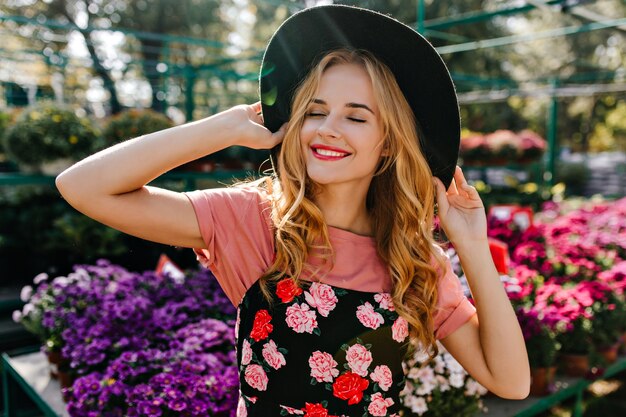 Gorgeous white woman in hat smiling on orangery. portrait of cheerful woman enjoying gardening.