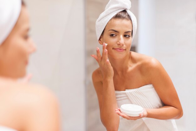 Gorgeous woman applying moisturizer on face