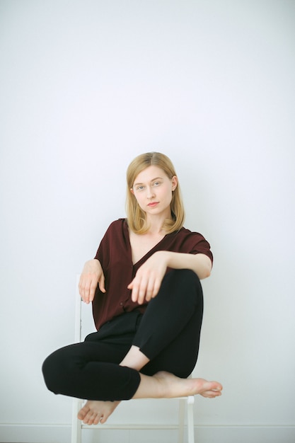 Free photo gorgeous woman in brown shirt and black pants sitting on a chair and looking in room with white background.