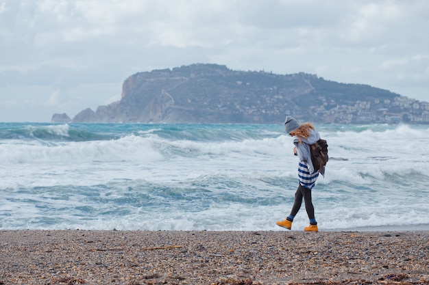 灰色のパーカーと帽子と海で昼間の間にビーチを歩いてゴージャスな女性