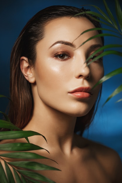 Gorgeous woman with beautiful fresh make up. Behind green leaves.