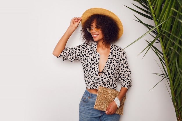 Free photo gorgeous woman with dark skin  in jeans and straw hat posing in studio over white background with  bag in bali style. sopping  mood.