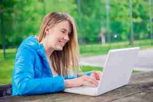 Free photo gorgeous young brunette girl using her laptop in sunlit park.