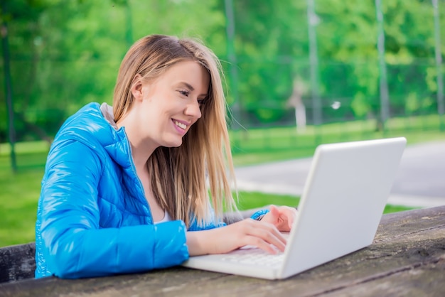 Gorgeous young brunette girl using her laptop in sunlit park.