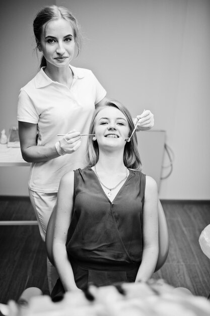 화려한 젊은 여성 치과 의사가 특수 장비를 갖춘 캐비닛에서 환자의 치아를 확인하는 흑백 사진