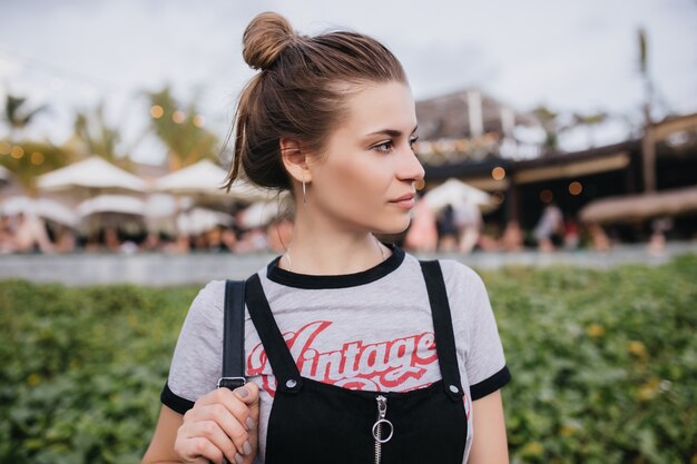 Gorgeous young female model posing on blur city. Portrait of magnificent girl with casual hairstyle waiting friends on the street near lawn.