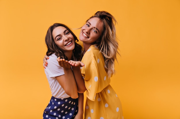 Gorgeous young girls expressing happy emotions. Indoor portrait of fascinating white female models standing on yellow.