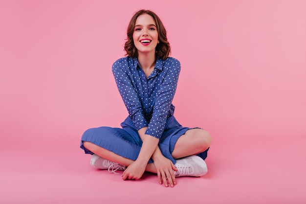 Gorgeous young lady sitting on the floor with cute smile. dreamy brunette girl in blue blouse enjoying photoshoot.