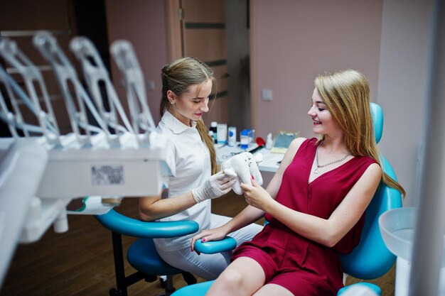 Gorgeous young orthodontist posing with big tooth model next to her pretty patient