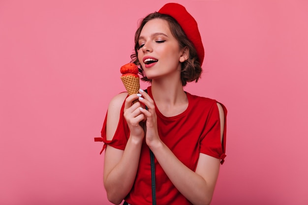 Splendida giovane donna in abiti rossi, mangiare il gelato. raffinato modello femminile francese in posa con il dessert.