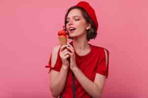 Foto gratuita splendida giovane donna in abiti rossi, mangiare il gelato. raffinato modello femminile francese in posa con il dessert.