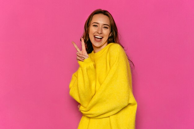 Великолепная молодая женщина, показывая мир жест, одетый в желтый свитер.