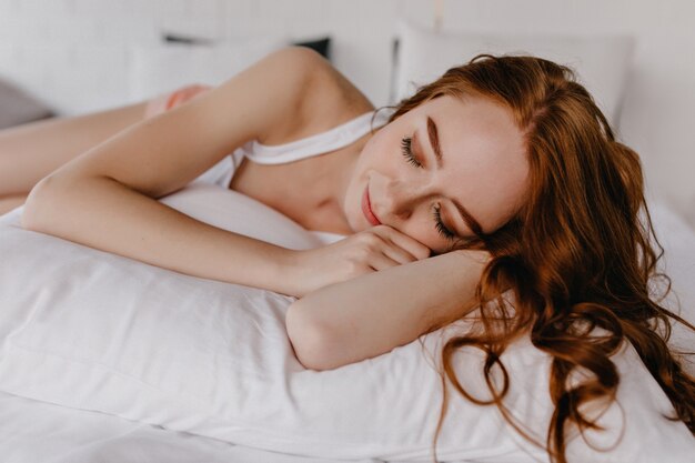 Gorgeous young woman with curly hairstyle sleeping in her room. Fascinating white girl lying on pillow with eyes closed.