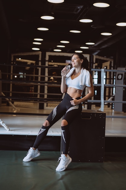 Gorgeous young woman with a towel on her shoulders drinking water from a bottle at the gym