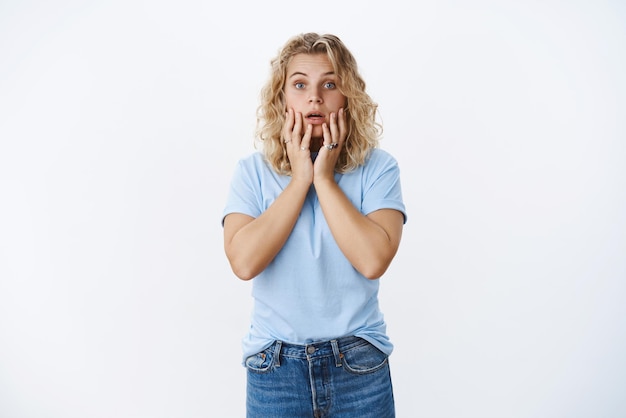 Free photo gosh what happened to you girl showing empathy and worry as looking with pitty at camera open mouth and raising eyebrows from shock holding hands anxious over lips against white background