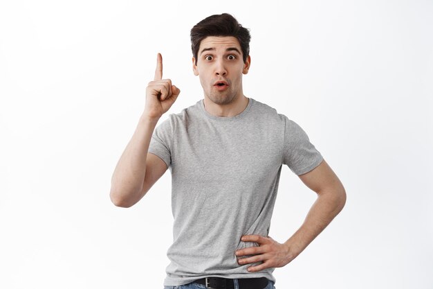 Got an idea. Excited handsome guy found solution, raising finger and say suggestion, have a plan, pointing up, standing over white background