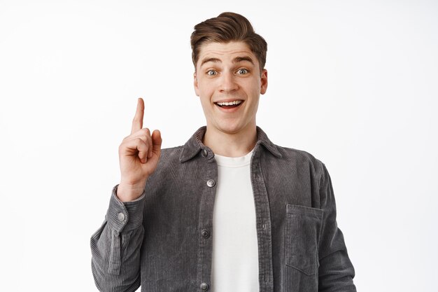 Got an idea. Excited young man has solution, raising finger eureka sign and smiling amazed, tell plan, pointing up, has suggestion, standing over white background