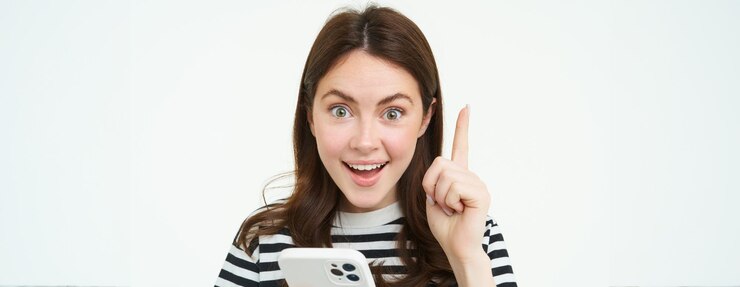 無料Photo 笑顔の女性が指を上げてスマートフォンを持っていると、何かがエウレカになることを示唆しているというアイデアを思いつきました