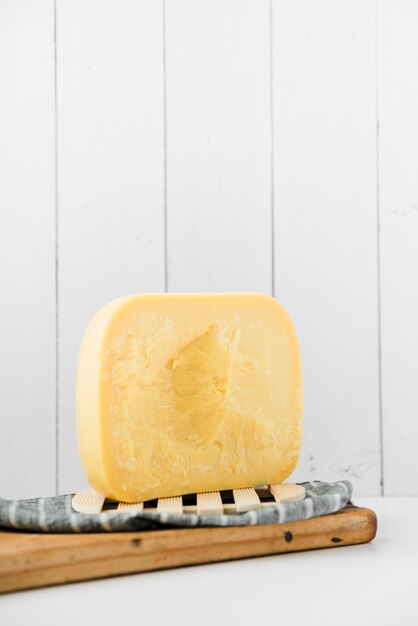 Gouda cheese on wooden chopping board against white wall