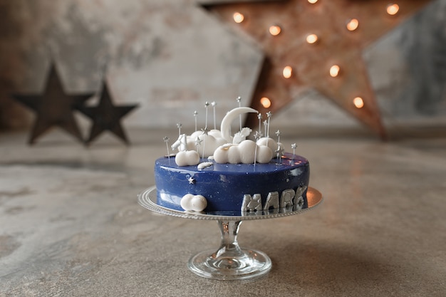 Изысканный синий торт ко дню рождения с белым декором и свеча номер один на стеклянной подставке на чердаке