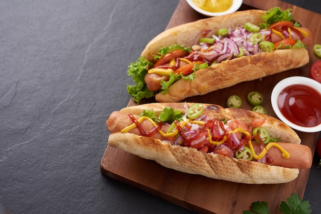 Foto gratuita hot dog di manzo alla griglia gourmet con lati e patatine. deliziosi e semplici hot dog con senape, pepe, cipolla e nachos. hot dog completamente caricati con condimenti assortiti su una tavola da paddle.