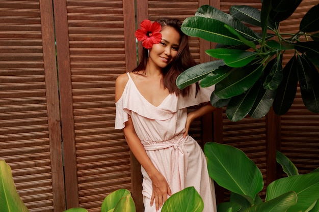 Graceful Asian woman with perfect skin  and hibiscus flower in hairs posing over wood wall