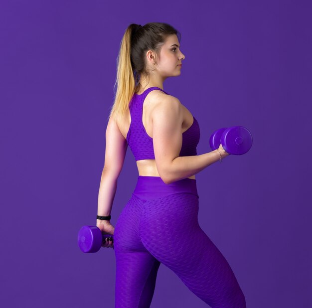 Graceful. Beautiful young female athlete practicing , monochrome purple portrait. Sportive fit caucasian model with weights. Body building, healthy lifestyle, beauty and action concept.