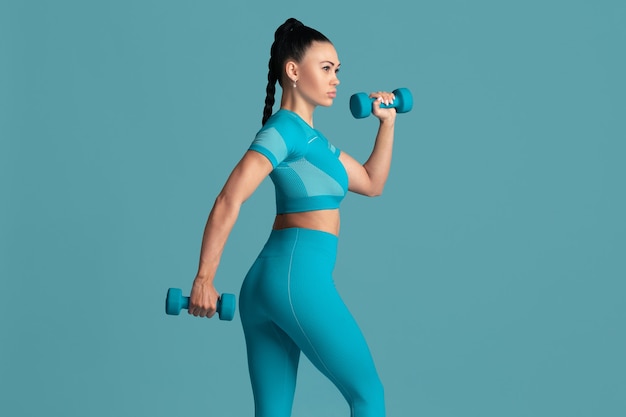 Graceful. Beautiful young female athlete practicing in studio, monochrome blue portrait