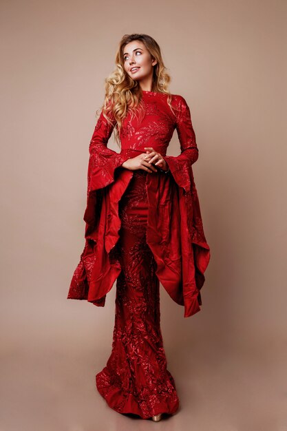 Graceful Blonde woman in elegant new year dress posing. Unusual wide sleeves. Wavy hairs. Full height. 