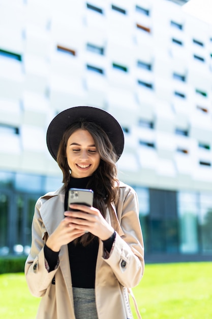 Graceful brunette woman in coat walking down the street with phone in hand.