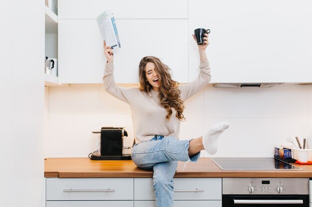 Graceful caucasian girl wears jeans enjoying good morning in her kitchen