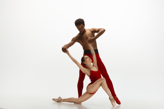 Graceful classic ballet dancers dancing isolated on white studio background. Couple in bright red clothes like a combination of wine and milk. The grace, artist, movement, action and motion concept.