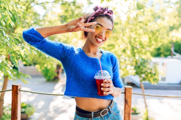 Graceful cute  girl showing signs by hands and holding tasty lemonade.