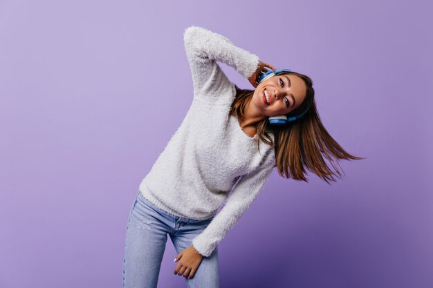 Graceful, energetic girl with short, smooth hair moves her torso while listening to her favorite song. Full-length portrait of European model on lilac