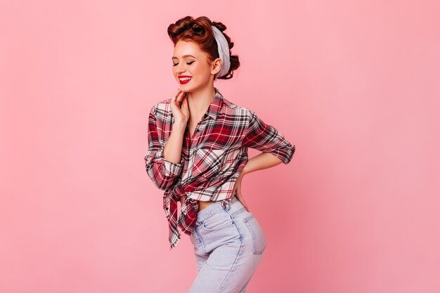 Graceful fit girl in checkered shirt standing on pink space. Studio shot of dancing pinup woman.