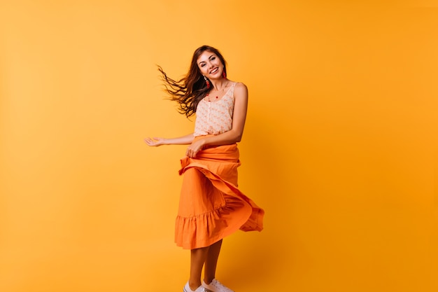 Graceful girl playing with her bright summer skirt. Indoor portrait of relaxed young woman dancing in studio.