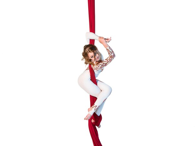 Graceful gymnast performing aerial exercises with red fabrics on white background