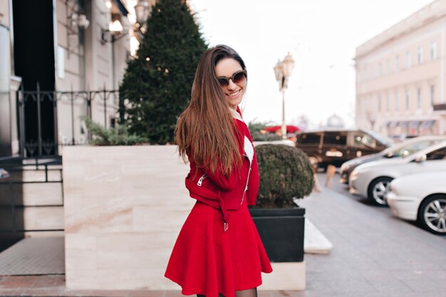 Graceful long-haired girl in trendy red skirt expressing sincere positive emotions