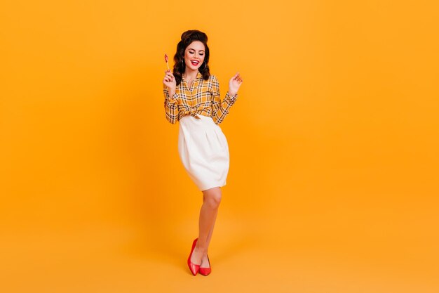 Graceful pinup girl expressing positive emotions Studio shot of stylish curly young woman posing on yellow background