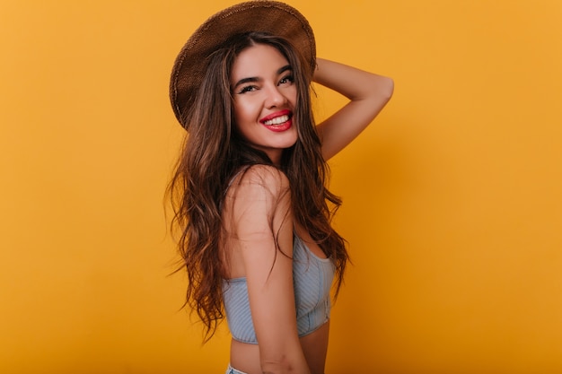 Graceful tanned woman in stylish brown hat standing in confident pose and smiling