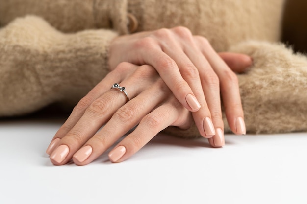 Graceful thin fingers of a girl with a trendy pastel nude manicure and a fluffy soft sweater and a cute silver ring bow